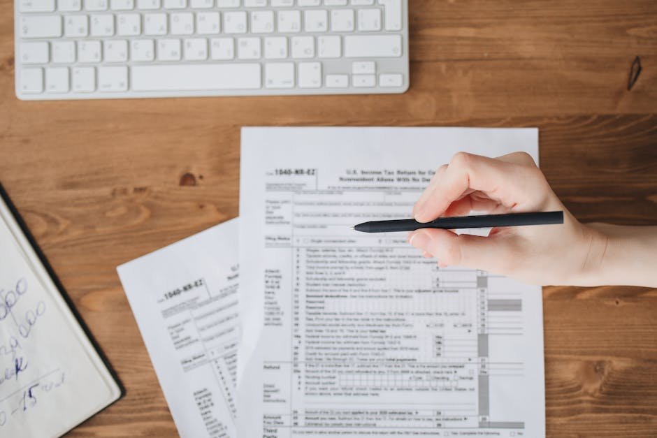 台馬跨境稅務：Close-up of a hand holding a pen over US tax forms on a wood